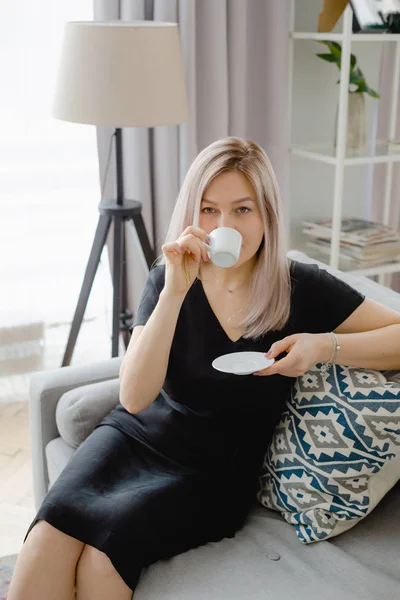 Mujer rubia en un vestido negro bebe café — Foto de Stock