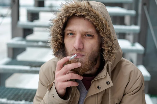 Un jeune homme barbu fume une cigarette en hiver — Photo