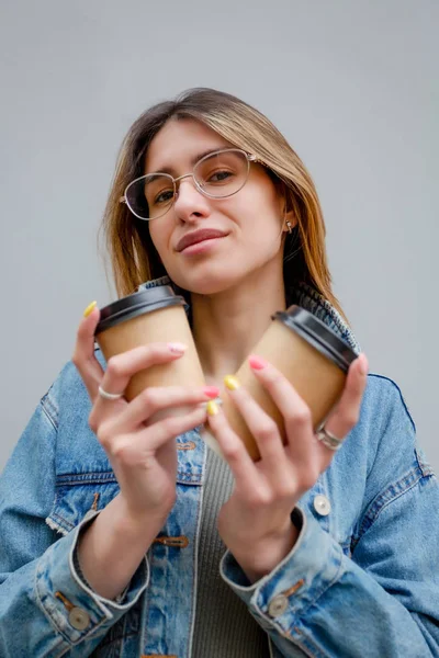 Blondes Mädchen mit Pappbechern Kaffee auf Grau — Stockfoto