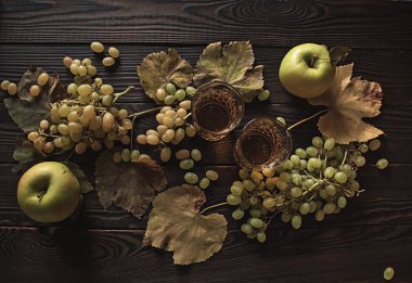 İki kristal bardak beyaz şarap, elma, üzüm ve kuru yaprakları bir ahşap yüzeyde. Üstten görünüm