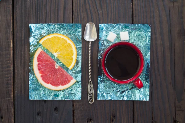 Orange slice and a cup of coffee on stands made of yellow and turquoise foil on a wooden surface