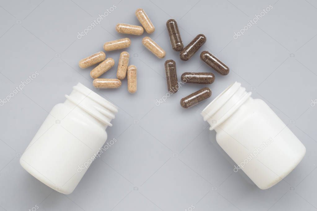 Medicinal capsule spill out of a two plastic bottles on a light surface