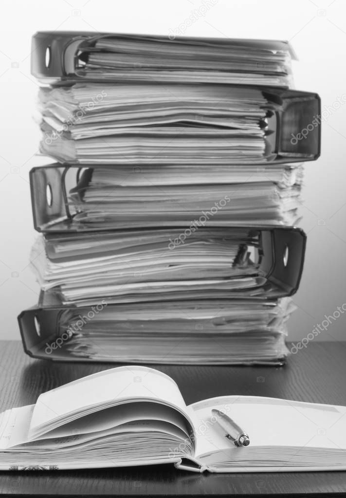 Seven Five folders with documents stacked in a pile on the table. Black and white photo