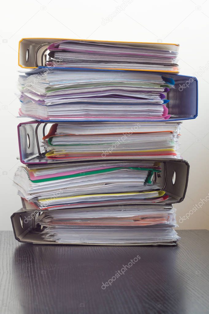 Five folders with documents stacked in a pile on the table. White background