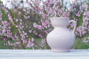 Porselen pembe sürahi bir tabloda çiçekli çalı arka planı beyaz tahtalar