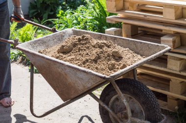 Bir adam kil el arabası içinde taşır
