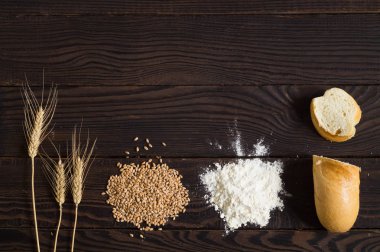Buğday kulaklar, tahıl, un ve koyu ahşap bir masa üzerine dilimlenmiş ekmek. Üstten görünüm