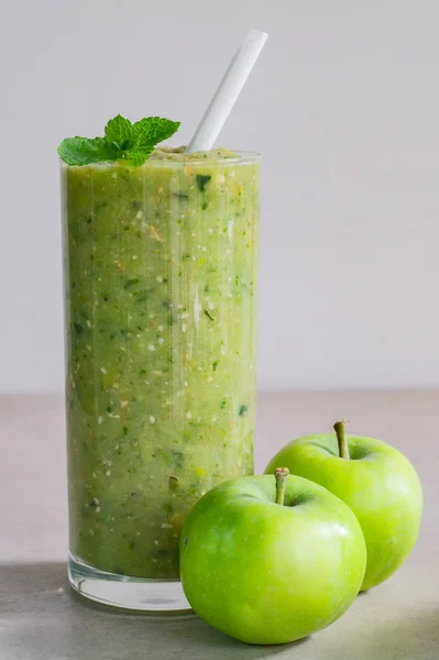 Green apple smoothie in a glass and two whole apples