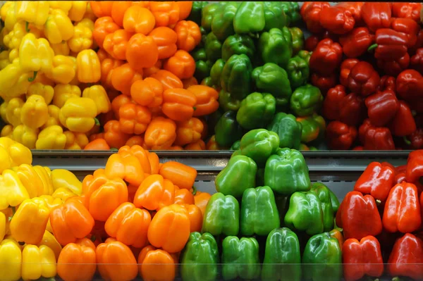 Red, yellow, orange and green vegetable peppers on the shelf in