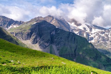 Yeşil dağ vadisi ve bulutlarda karlı dağ yamaçları, Aus
