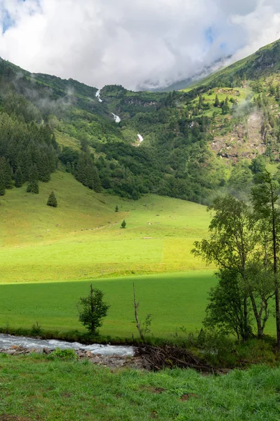 Alpské údolí a vodopád se zelenou trávou a horami v th — Stock fotografie