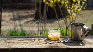 Ahşap bir masada metal bardak ve bal kavanozu.
