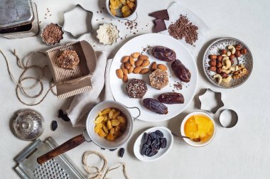 Beyaz bir tabakta hurma, fındık, bal ve kuru üzümlerden elde edilen doğal faydalı tatlılar. Bu malzemeler masanın üstünde.