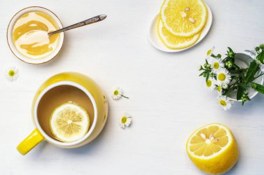 Sarı fincanda limon çayı, yarım limon ve papatya çayı.