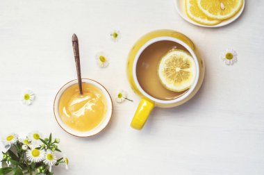 Sarı fincanda limon çayı, yarım limon ve papatya çayı.