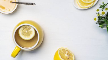 Sarı fincanda limon çayı, yarım limon ve papatya çayı.