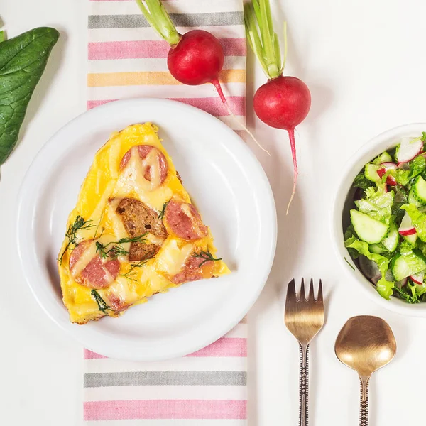 Tortilla con croutons, salchichas, queso y eneldo en un plato blanco y ensalada de verduras — Foto de Stock