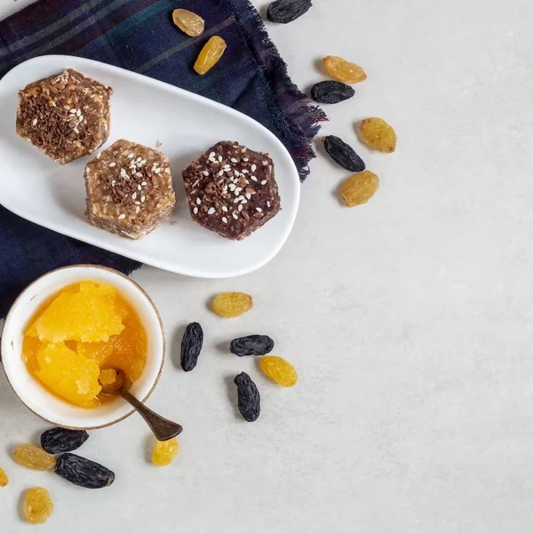 Healthy sweets made from natural ingredients on a white plate. Near honey, yellow and dark blue raisins