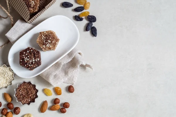 Healthy sweets made from natural ingredients on a white plate. Near nuts, sesame and raisins