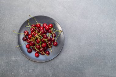 Gri arkaplanda siyah bir tabakta kırmızı kirazlar