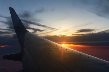 Gün batımında ya da gündoğumunda güneşin arka planında uçan bir uçağın kanadı.