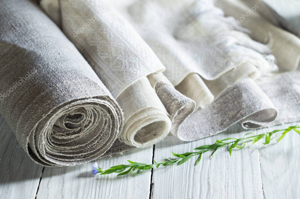 Old homespun and modern factory linen fabrics in rolls and blooming flax on a white wooden table