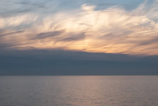 Gray, white and orange clouds on the blue sky above the sea at sunrise