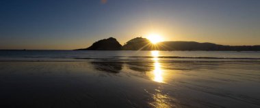 Zurriola beach, güneşin arkasında dağlar içinde şehir San Sebastian, Bask Ülkesi.