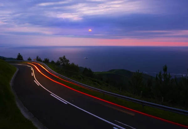 Car lights on the road, near the coast with the sun at sunset and the sea in the background