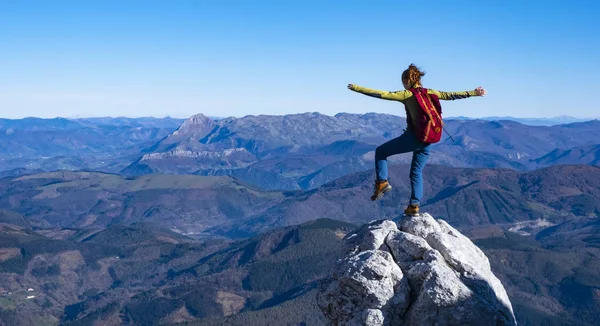 Happy celebrating winning success woman with arms raised in of having reached mountain top summit goal during hiking travel trek.