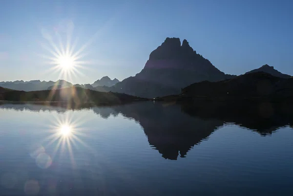 The sun and the Midi d\'Ossau peak are reflected in Lake Gentau at dawn, Pyrenees of France