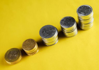 Parlak sarı arkaplandaki bozuk para yığınları finansal büyüme ve tasarrufları temsil ediyor. Bu kompozisyon yatırım, ekonomi ve parasal planlama gibi kavramlar için idealdir..