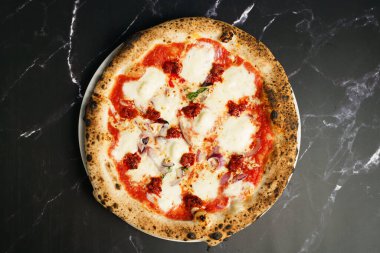 Eritilmiş mozzarella, domates sosu, kırmızı soğan ve baharatlı kırmızı pesto dilimleriyle kaplı taze pişmiş Napoli usulü pizzanın genel manzarası..