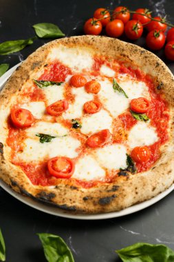 Çeri domatesli, erimiş mozzarella ve canlı fesleğen yapraklı hakiki Napoli pizzası. Bir demet taze domates ve saçılmış fesleğen yaprağı..