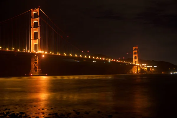 San Francisco, California, Verenigde Staten-25 november 2018: Golden Gate Bridge gezien vanaf Fort Point Overlook is gloeiend in de nacht met ster paden in de lucht erachter — Stockfoto