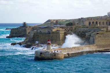 VALLETTA, MALTA - DEC 31st, 2019: View from Fort St Elmo on to the Ricasoli Grand Harbour East Breakwater and red lighthouse during strong waves