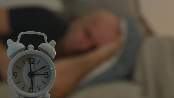 Focus Foreground Image with Alarm Clock and Tired Person Sleeping in Background