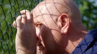 Üzgün ve kızgın adam metalik bir çitin arkasından bakan