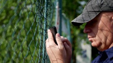 Adam bir akıllı telefon kullanılan bir metal çit metnin arkasına