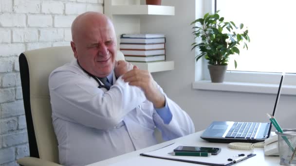 筋肉痛に苦しんでのオフィスの机の上に座って疲れた医者が彼の肩をマッサージします — ストック動画