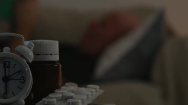 Tıbbi hapları ve ön plan ve kanepe üzerinde uyuyan bir adam bir çalar saat bulanıklığı
