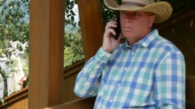 Rahat çiftçi bir ahşap salıncak sandalyede Dengeleme cep telefonunuza konuşmak ve mutlu gülümseme