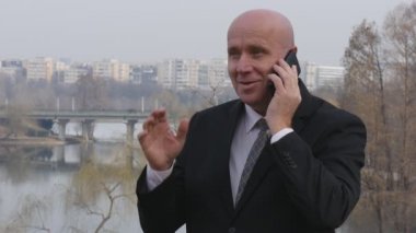 Ağır çekim Park gülümseyen iş adamı ile cep telefonu ve el hareketi için konuşun