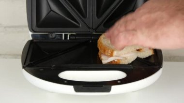 Adam jambon füme ve elektrikli ızgara kullanarak ekmek ile kavrulmuş sandviç hazırlama