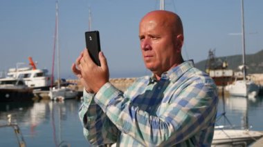 Memnun turist gülümseme ve kişisel cep telefonu kullanarak bir limanda fotoğraf çekmek