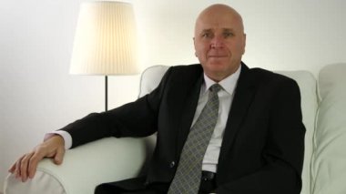 Kanepede oturan ve kamera için memnun gülümseyen iş adamı sunum