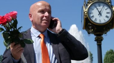 Mutlu bir insan memnun Talk cep telefonu gülümseme ve bir gül buketi bir bayanla bekleyin