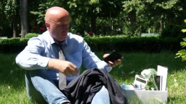 Park aşağı yeşil çim ve cep telefonunuza onun hakkında konuşurken oturan adam ateş