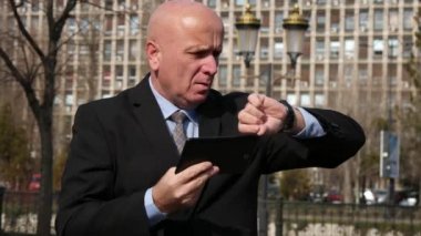 İşadamı sokakta zaman kontrol ve geç bir toplantı bekliyor Tablet kullanma.