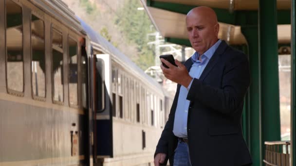 Бизнесмен Разговаривает Мобильным Телефоном Железнодорожной Станции Рядом Пассажирской Платформой — стоковое видео
